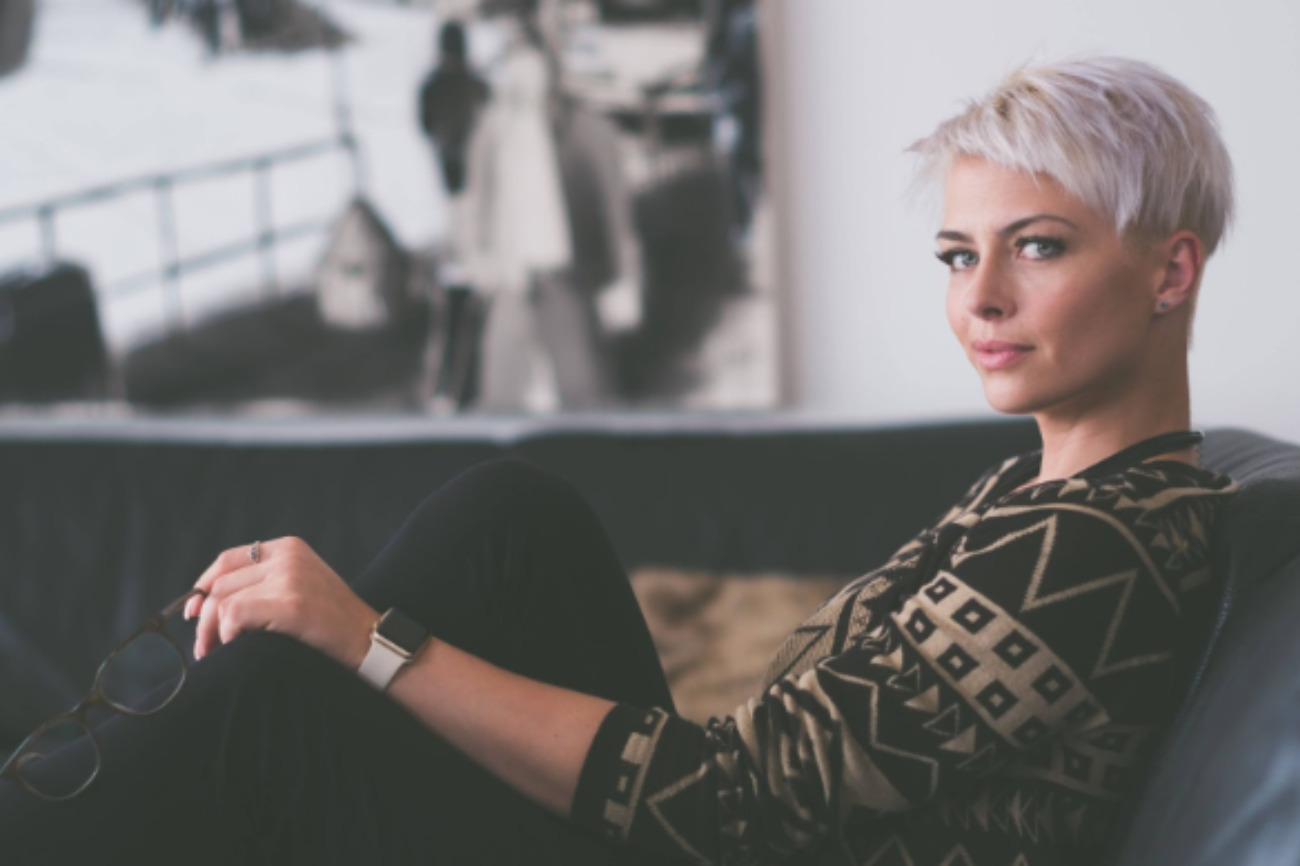 woman with blonde 90s hairstyles pixie haircut sat on sofa