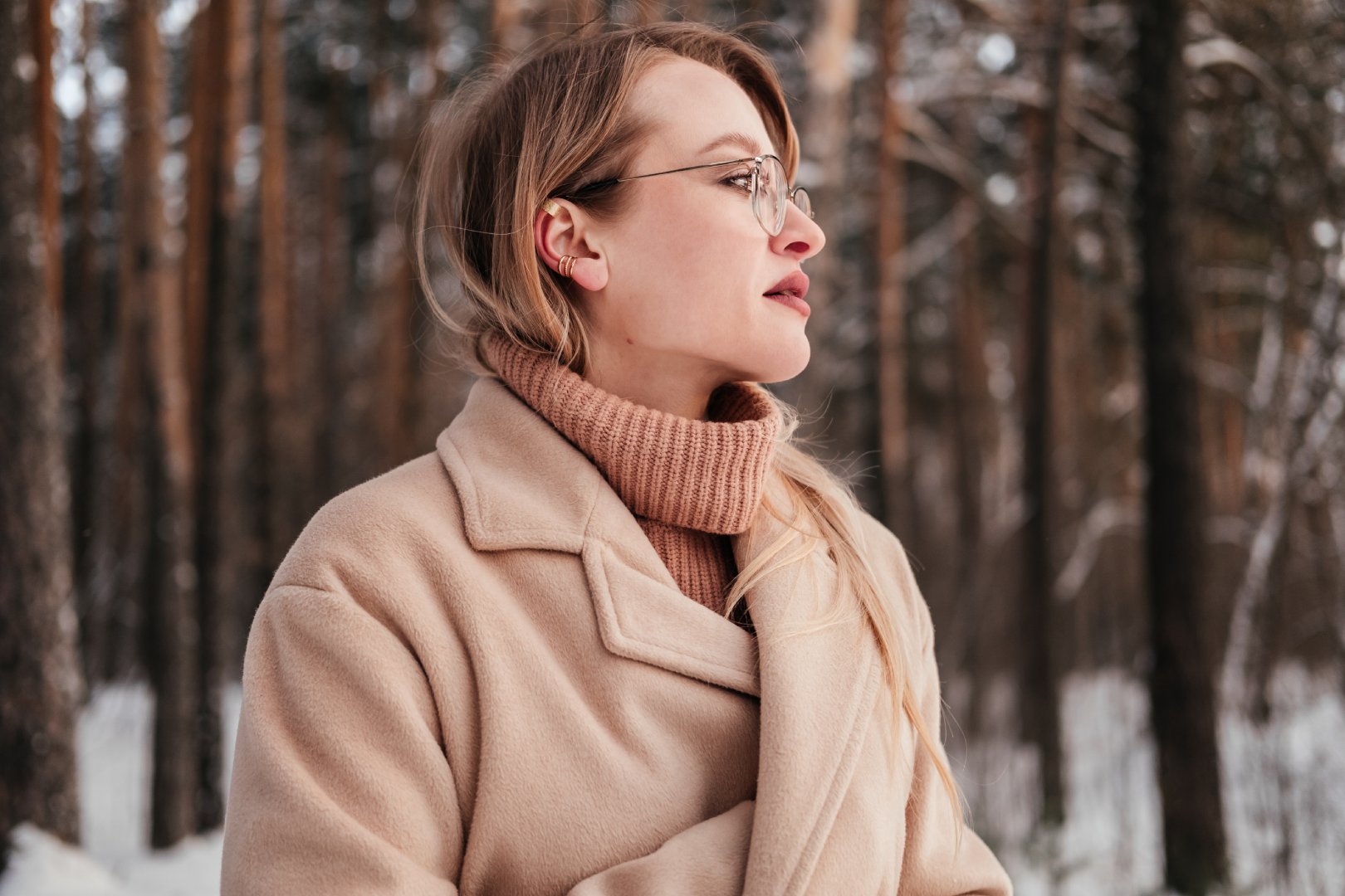Face profile of mid age woman in coat and sweater standing in winter forest outdoors. Blonde girl in eyeglasses